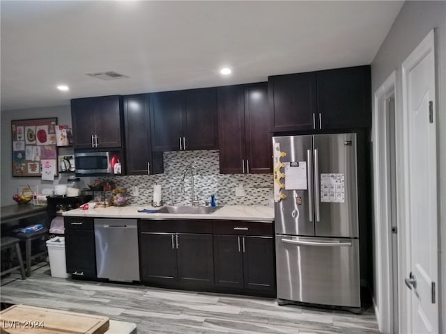 kitchen featuring dark brown cabinetry, sink, light hardwood / wood-style flooring, decorative backsplash, and appliances with stainless steel finishes