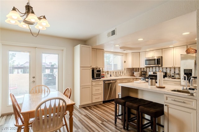 kitchen featuring sink, stainless steel appliances, light hardwood / wood-style floors, decorative backsplash, and decorative light fixtures