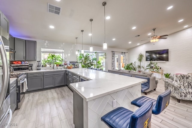 kitchen featuring stainless steel appliances, sink, gray cabinets, pendant lighting, and light wood-type flooring