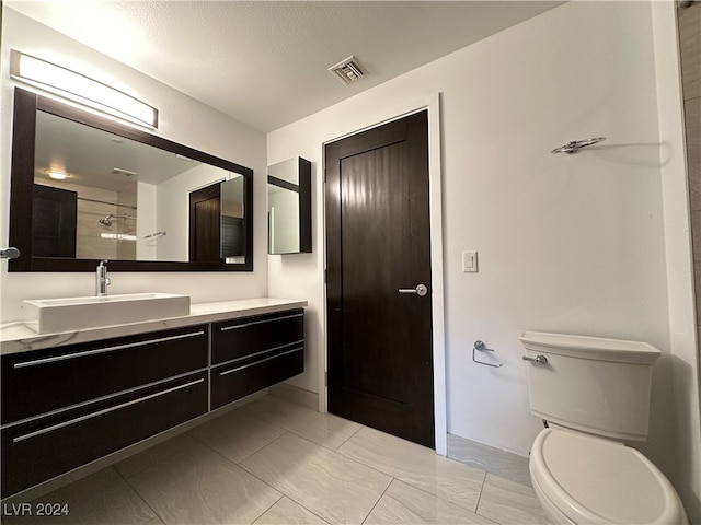 bathroom with tiled shower, vanity, a textured ceiling, and toilet