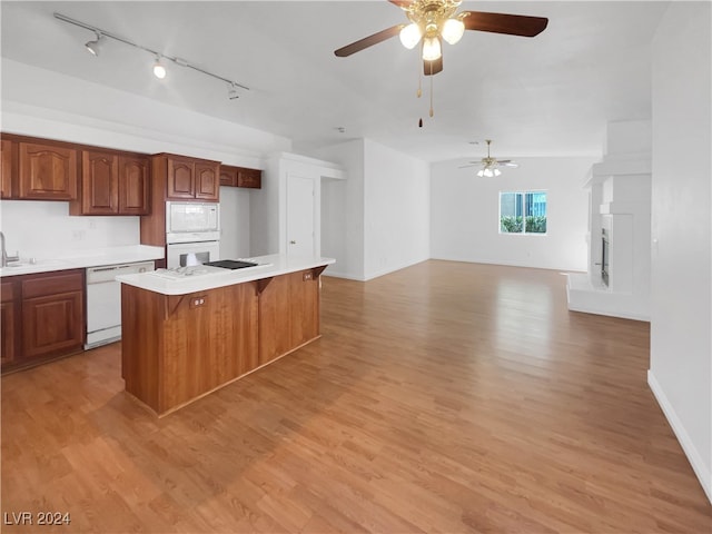 kitchen with light hardwood / wood-style floors, ceiling fan, a breakfast bar area, white appliances, and a kitchen island