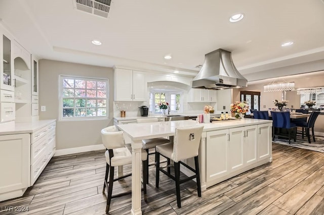 kitchen with island range hood, a healthy amount of sunlight, white cabinetry, and a center island