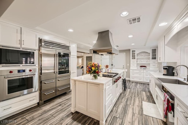 kitchen featuring built in appliances, island range hood, and white cabinetry