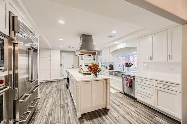 kitchen with stainless steel appliances, white cabinetry, island range hood, and a center island