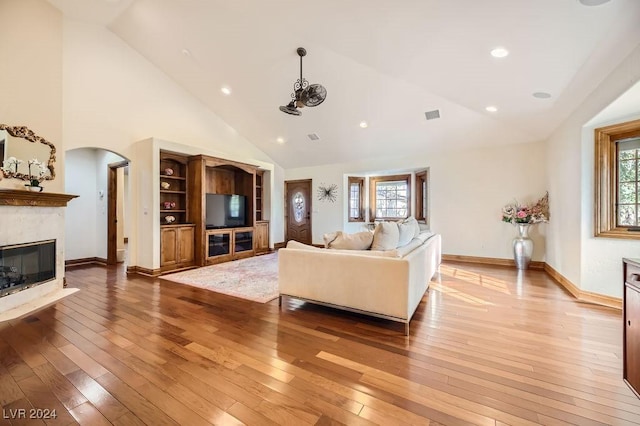 living room featuring a healthy amount of sunlight, high vaulted ceiling, light hardwood / wood-style flooring, and a high end fireplace