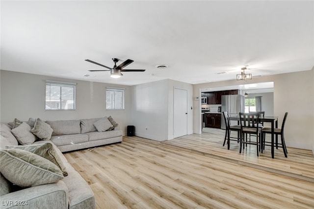 living room with ceiling fan with notable chandelier and light hardwood / wood-style flooring