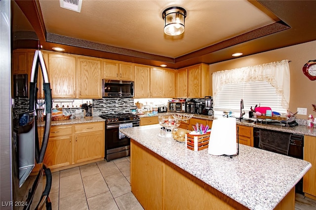 kitchen with appliances with stainless steel finishes, a tray ceiling, and light stone countertops