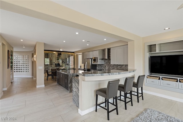 kitchen with tasteful backsplash, stainless steel appliances, gray cabinets, a kitchen breakfast bar, and wall chimney exhaust hood