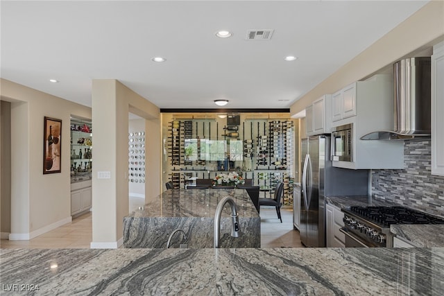 kitchen with dark stone countertops, white cabinetry, appliances with stainless steel finishes, and wall chimney exhaust hood