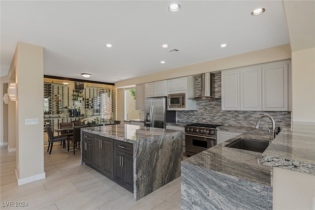 kitchen featuring stainless steel appliances, sink, light stone countertops, wall chimney exhaust hood, and a kitchen island