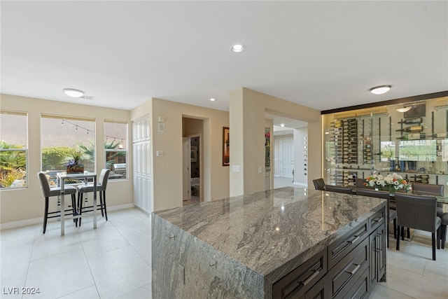 kitchen with dark brown cabinetry, dark stone countertops, light tile patterned floors, and a center island