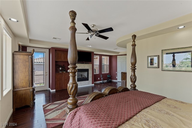 bedroom featuring access to outside, a fireplace, dark hardwood / wood-style floors, a tray ceiling, and ceiling fan