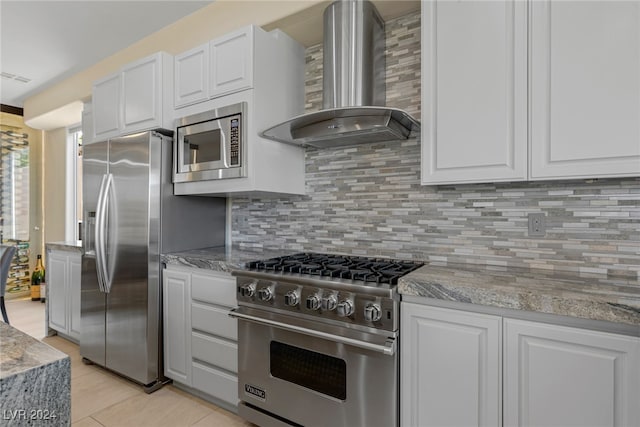 kitchen with stainless steel appliances, white cabinetry, light stone countertops, wall chimney exhaust hood, and backsplash