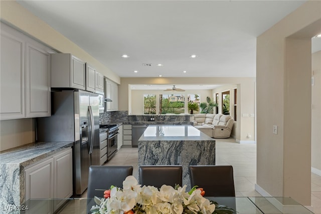 kitchen featuring stainless steel appliances, a center island, light tile patterned floors, ceiling fan, and backsplash