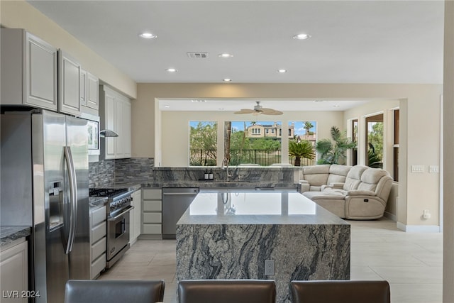 kitchen featuring stainless steel appliances, decorative backsplash, sink, ceiling fan, and a center island