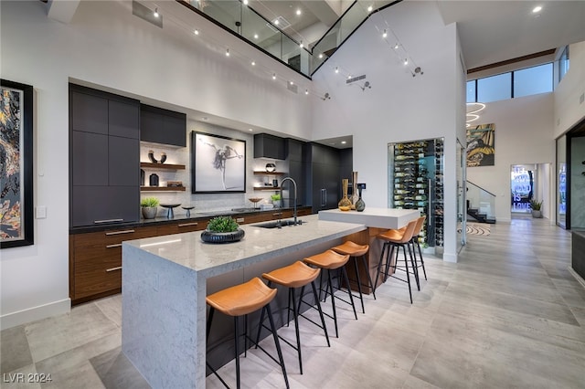 kitchen featuring a high ceiling, a large island with sink, sink, tasteful backsplash, and a kitchen bar