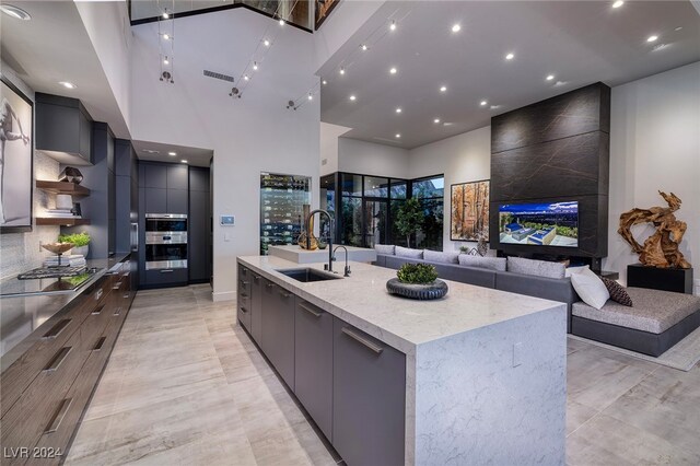 kitchen featuring light stone counters, a towering ceiling, gas stovetop, a large island with sink, and sink