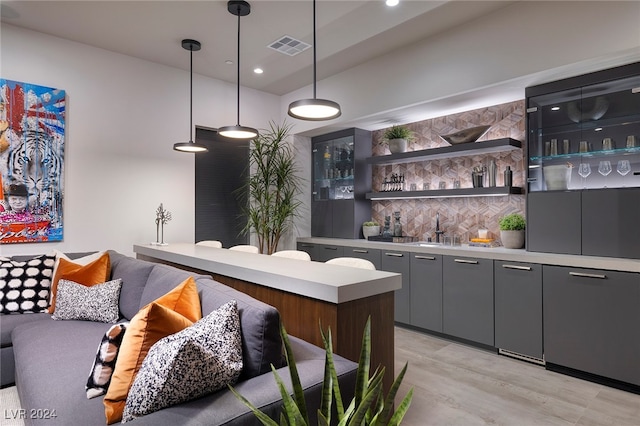 bar with decorative backsplash, sink, light hardwood / wood-style flooring, and decorative light fixtures