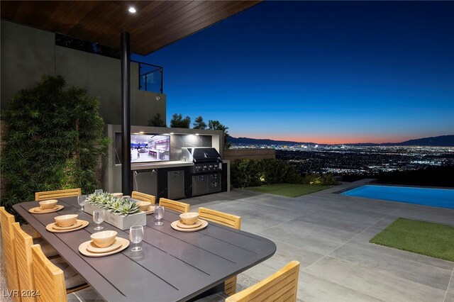 patio terrace at dusk featuring area for grilling, a fenced in pool, and grilling area