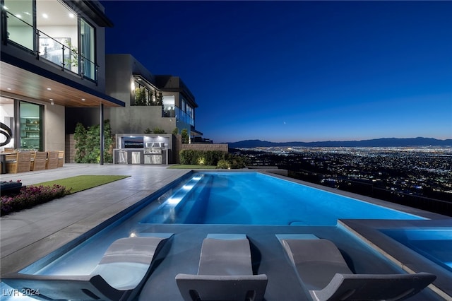 pool at dusk with a mountain view, area for grilling, and a patio