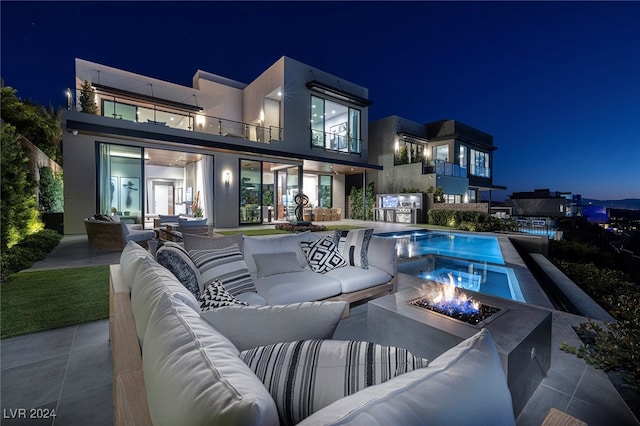 back house at twilight with an outdoor living space with a fire pit, a patio area, and a balcony