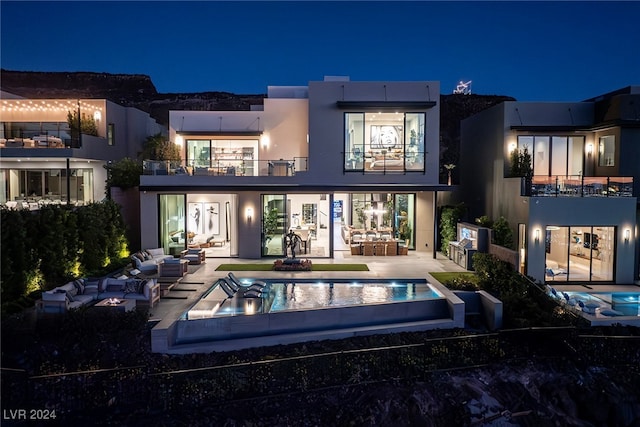 back house at night featuring a patio, an outdoor hangout area, and a balcony