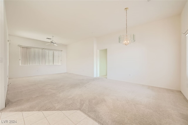 empty room featuring ceiling fan with notable chandelier and light colored carpet