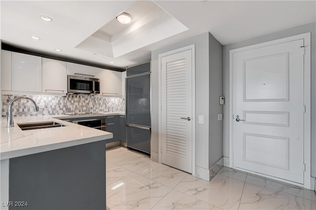 kitchen with built in refrigerator, white cabinetry, backsplash, a raised ceiling, and sink