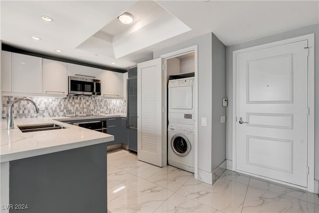 kitchen with gray cabinetry, stacked washer and dryer, decorative backsplash, sink, and white cabinets