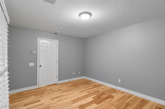 empty room featuring light wood-type flooring, visible vents, baseboards, and a textured ceiling