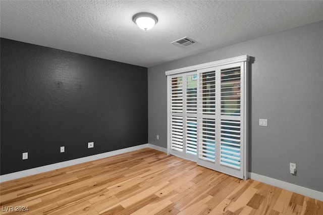 unfurnished room featuring a textured ceiling, wood finished floors, visible vents, and baseboards