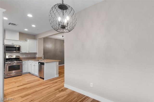 kitchen featuring light wood-style flooring, appliances with stainless steel finishes, white cabinets, a sink, and a chandelier