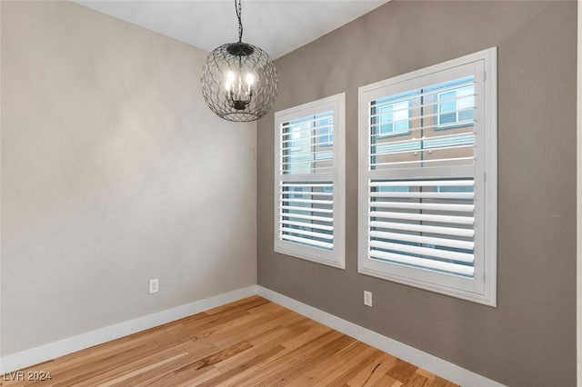 empty room with light wood-type flooring, plenty of natural light, baseboards, and a chandelier