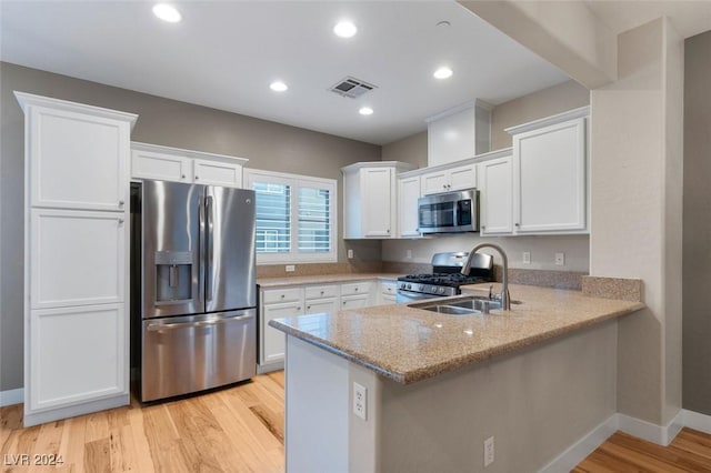 kitchen featuring light wood-style flooring, a peninsula, a sink, white cabinets, and appliances with stainless steel finishes