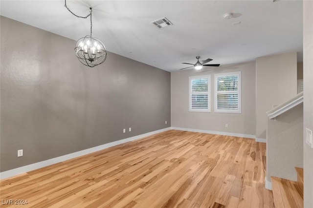 unfurnished living room featuring visible vents, stairway, wood finished floors, baseboards, and ceiling fan with notable chandelier