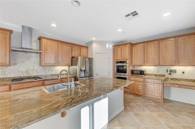 kitchen with sink, tasteful backsplash, wall chimney range hood, light stone countertops, and appliances with stainless steel finishes