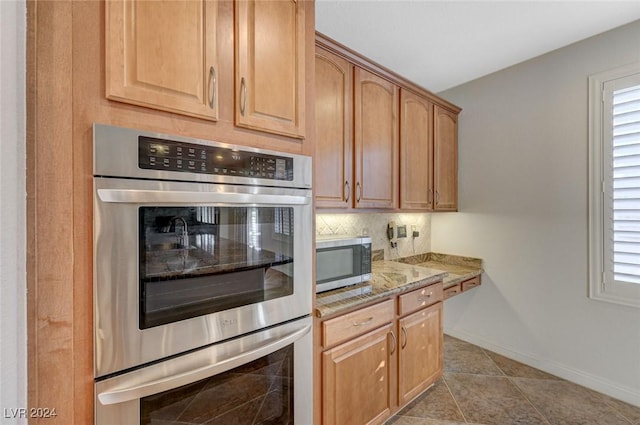 kitchen with light stone counters, stainless steel appliances, backsplash, and plenty of natural light