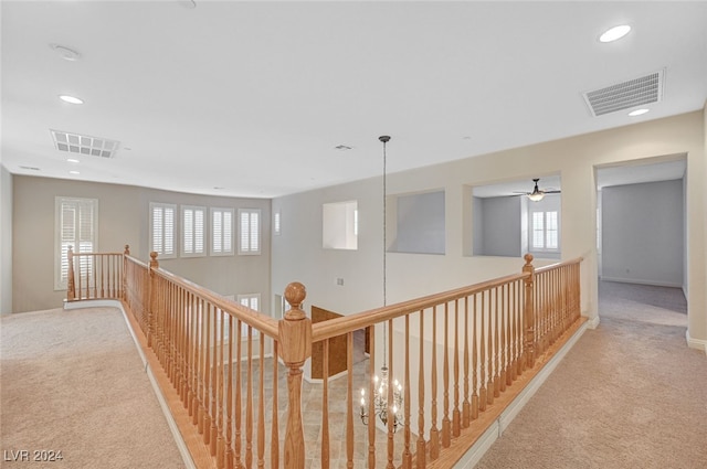 hall featuring a healthy amount of sunlight, light carpet, and an inviting chandelier