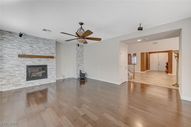 unfurnished living room featuring hardwood / wood-style flooring, a stone fireplace, and ceiling fan