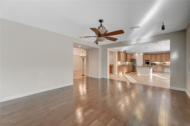 unfurnished living room with ceiling fan with notable chandelier and light wood-type flooring