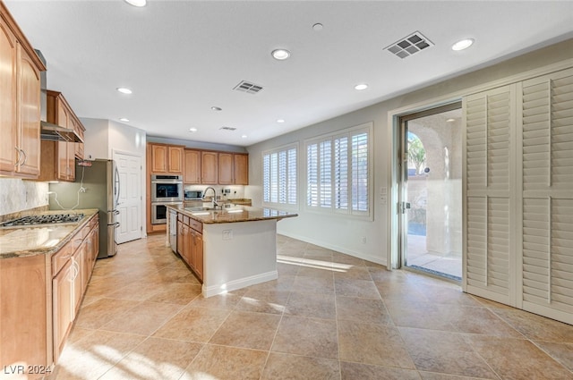 kitchen with light stone countertops, appliances with stainless steel finishes, sink, and an island with sink