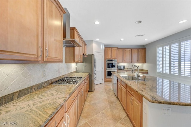 kitchen featuring wall chimney range hood, sink, appliances with stainless steel finishes, backsplash, and light stone counters