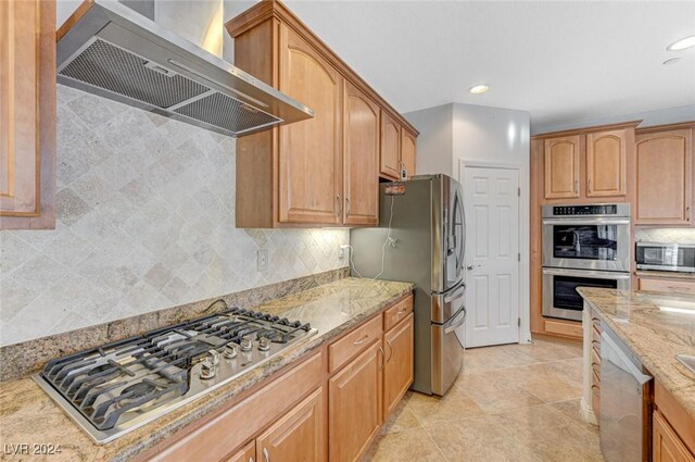 kitchen with light tile patterned floors, wall chimney range hood, backsplash, light stone countertops, and appliances with stainless steel finishes