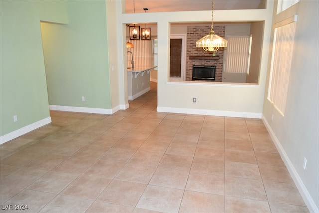 unfurnished living room featuring light tile patterned floors, a chandelier, and a brick fireplace