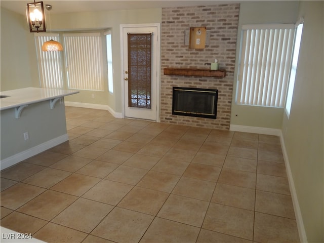 unfurnished living room featuring a brick fireplace, a healthy amount of sunlight, and light tile patterned flooring