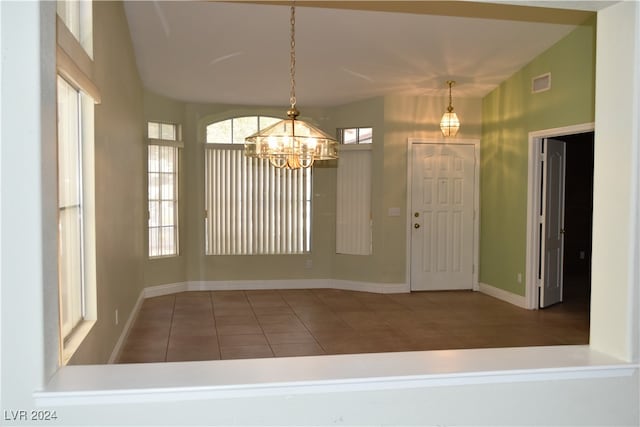 interior space with a notable chandelier, dark tile patterned floors, and vaulted ceiling