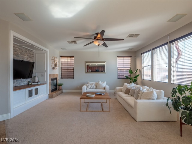 living room with a tiled fireplace, light colored carpet, and ceiling fan