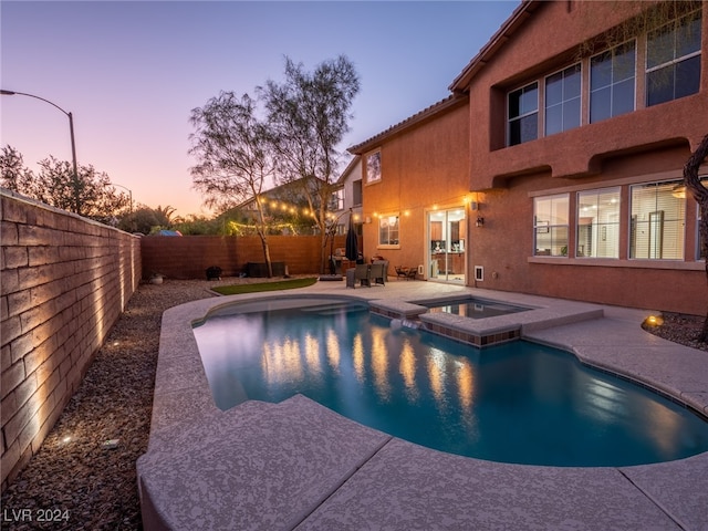 pool at dusk with an in ground hot tub and a patio area