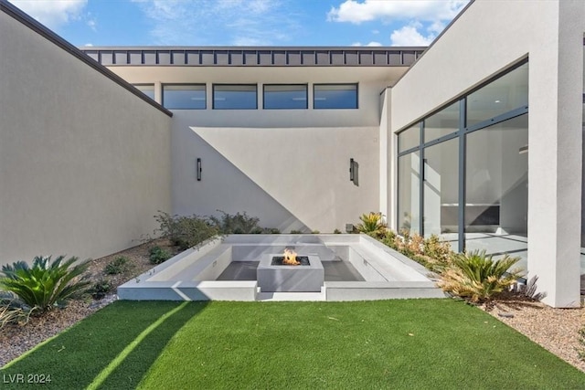 exterior space with stucco siding, a lawn, and an outdoor fire pit