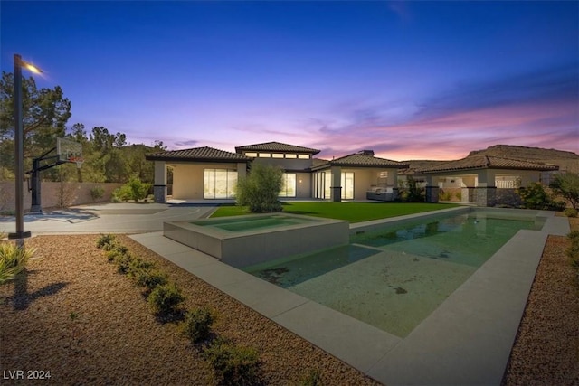 back of property at dusk with a patio, a tiled roof, an outdoor pool, and stucco siding